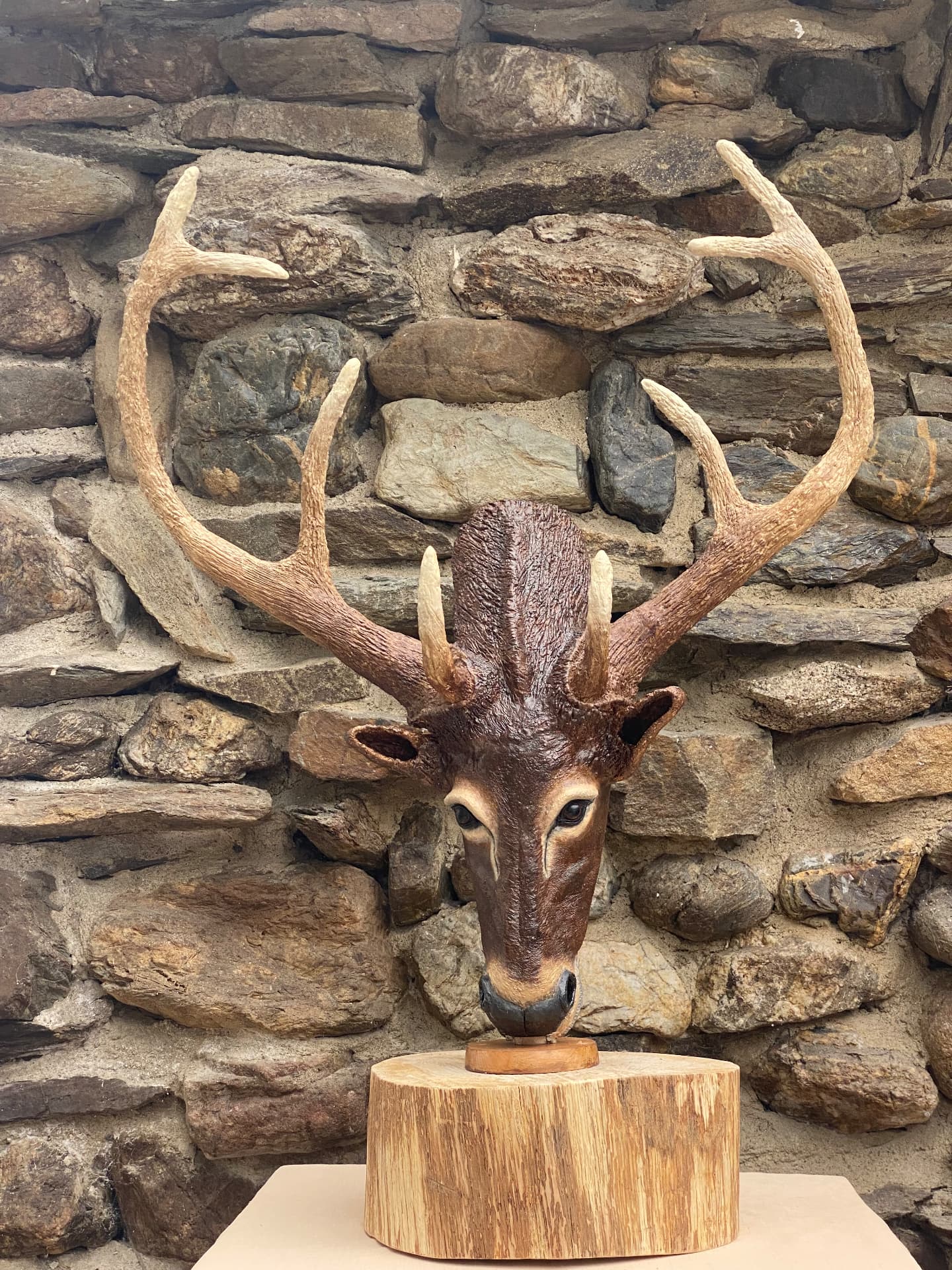 Hand-sculpted clay stag-head sculpture Spirit on a wooden plinth against a stone wall