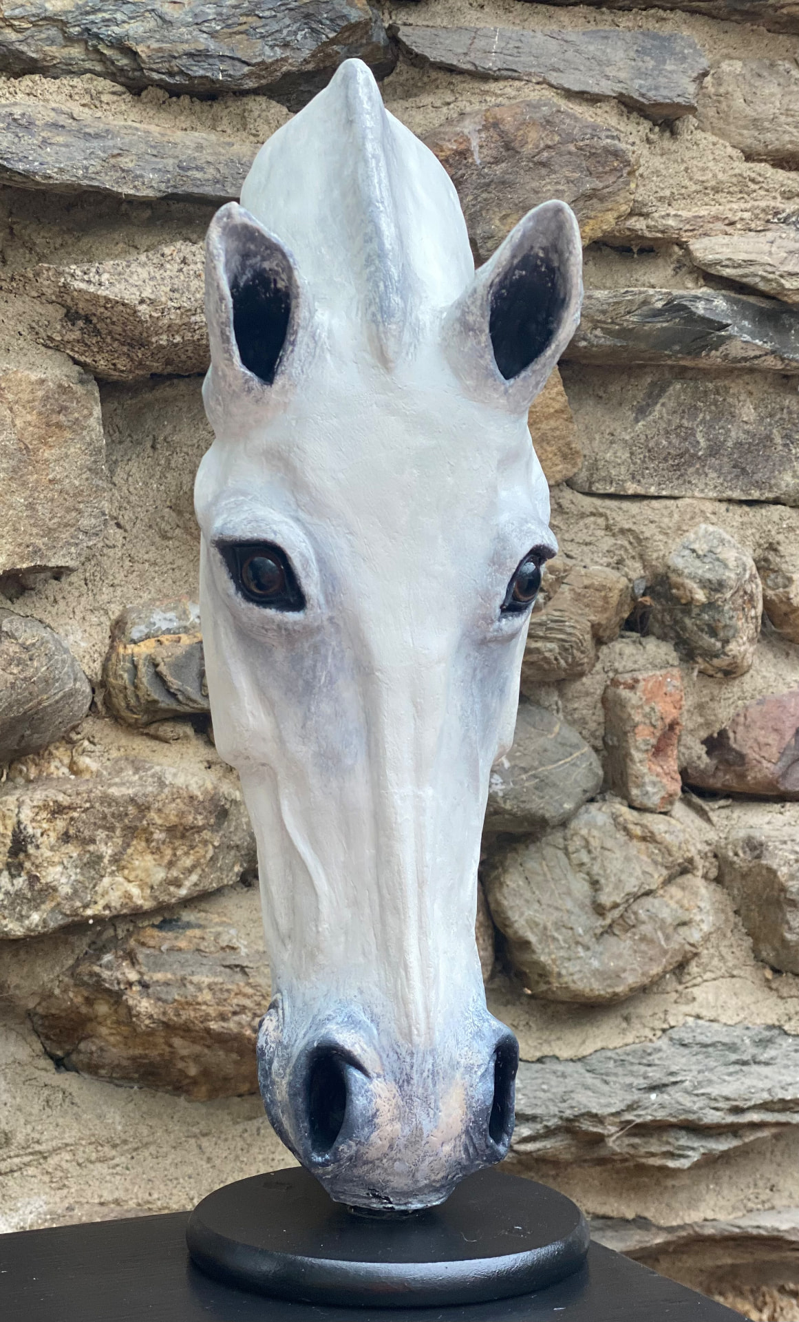 Hand-sculpted white horse-head sculpture of Soul Dawn, frontal view on a black plinth against a stone wall